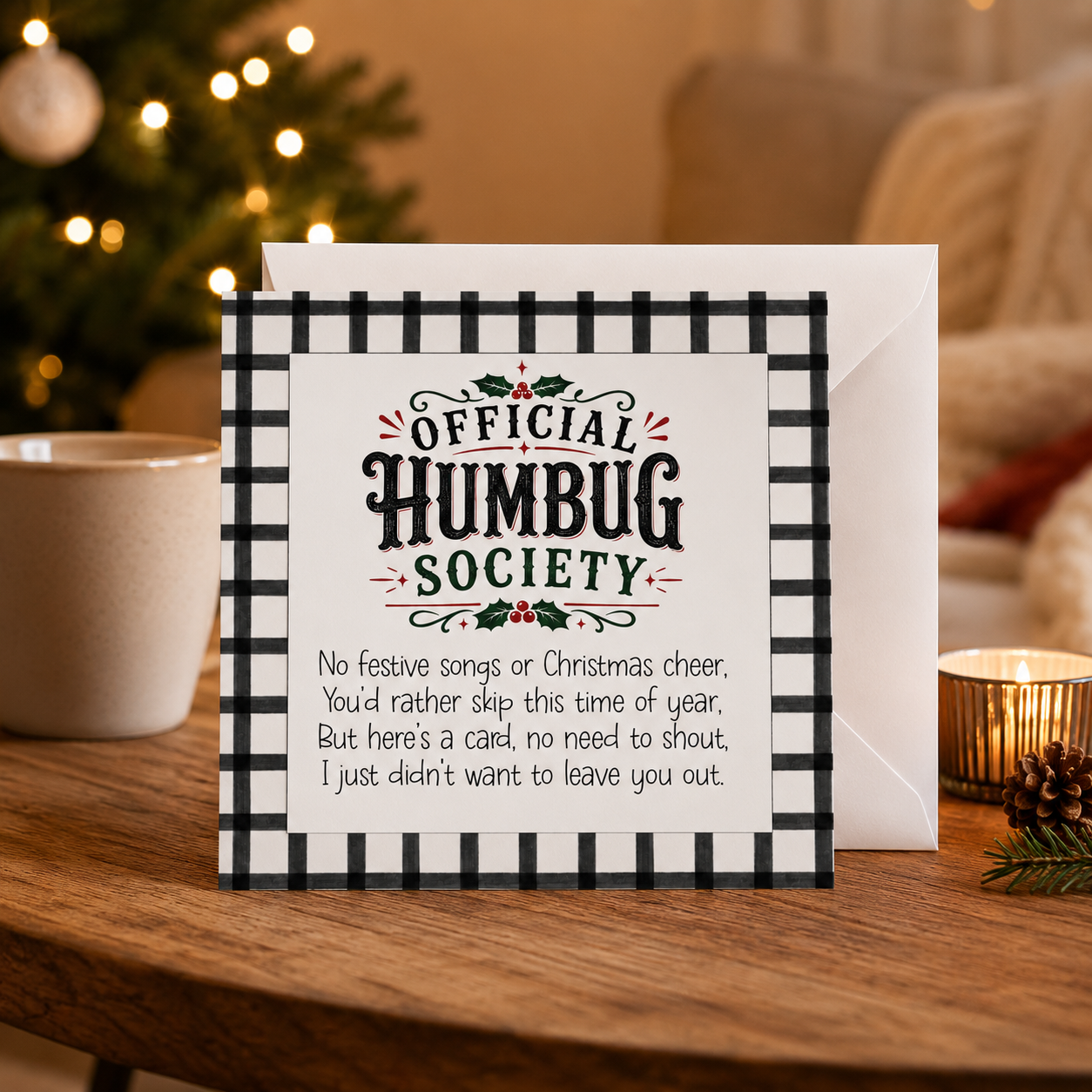 Rude funny Christmas card reading 'Official Humbug Society' on a black and white check background, styled on a coffee table with a Christmas tree