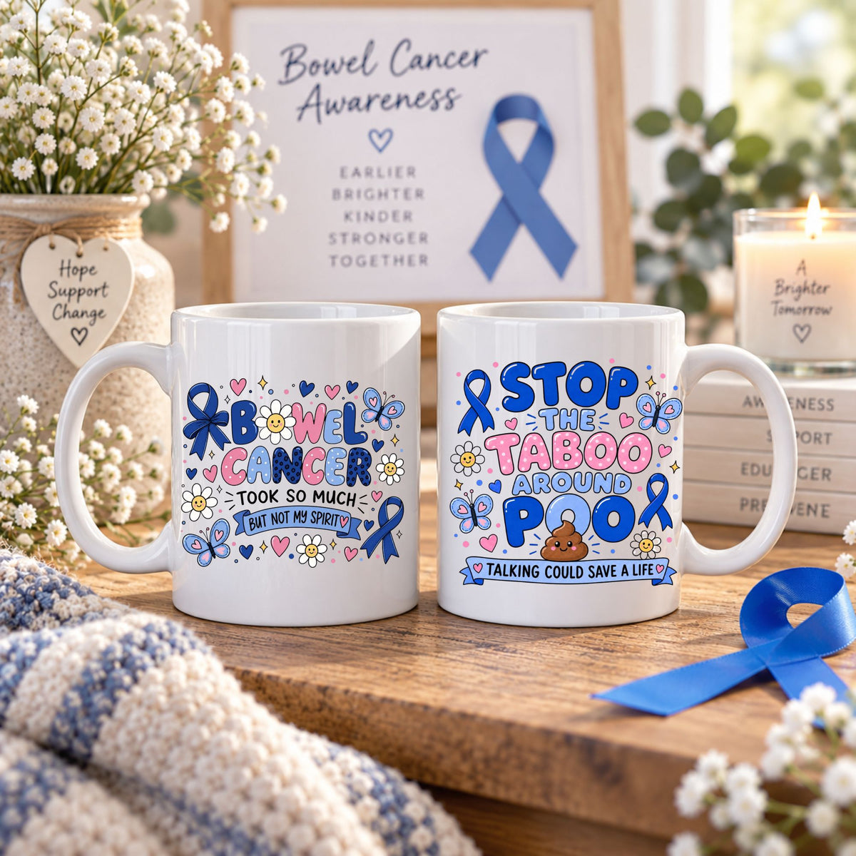 Two white ceramic mugs with colorful Bow Cancer Awareness-themed designs, displayed on a wooden surface with flowers, a candle, and a framed awareness sign in the background.