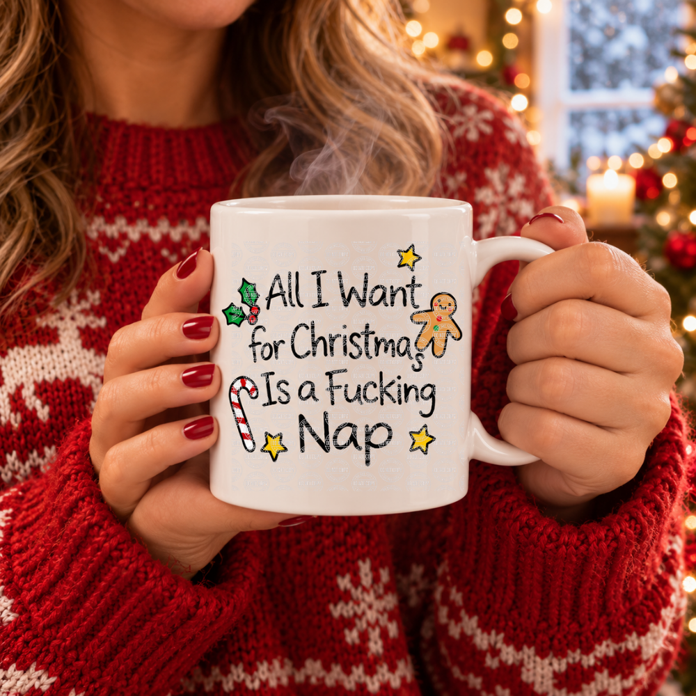 A person in a red knit sweater holds a white ceramic mug with a Christmas-themed printed message that reads 'All I Want for Christmas Is a Fucking Nap' with candy cane, gingerbread man, and star illustrations.