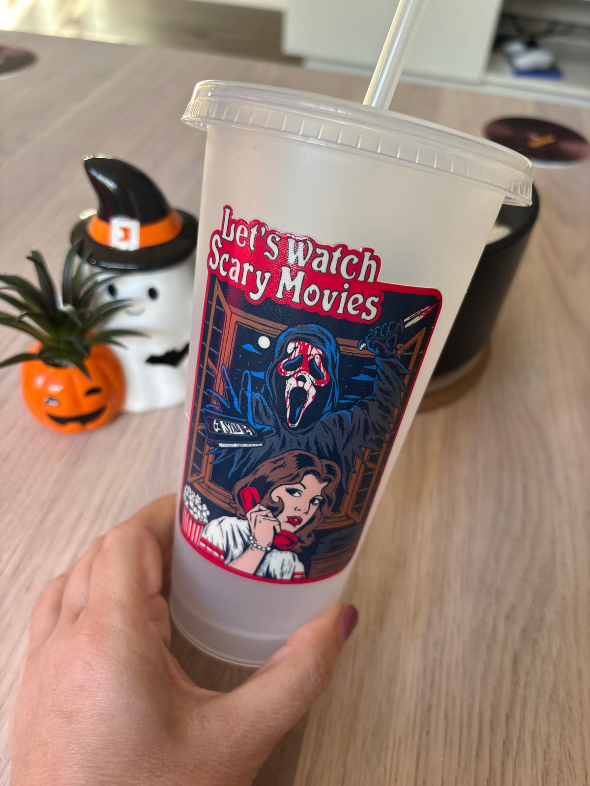 Close-up of frosted 24oz tumbler with a masked stalker, VHS tape and popcorn bucket in a retro horror poster design