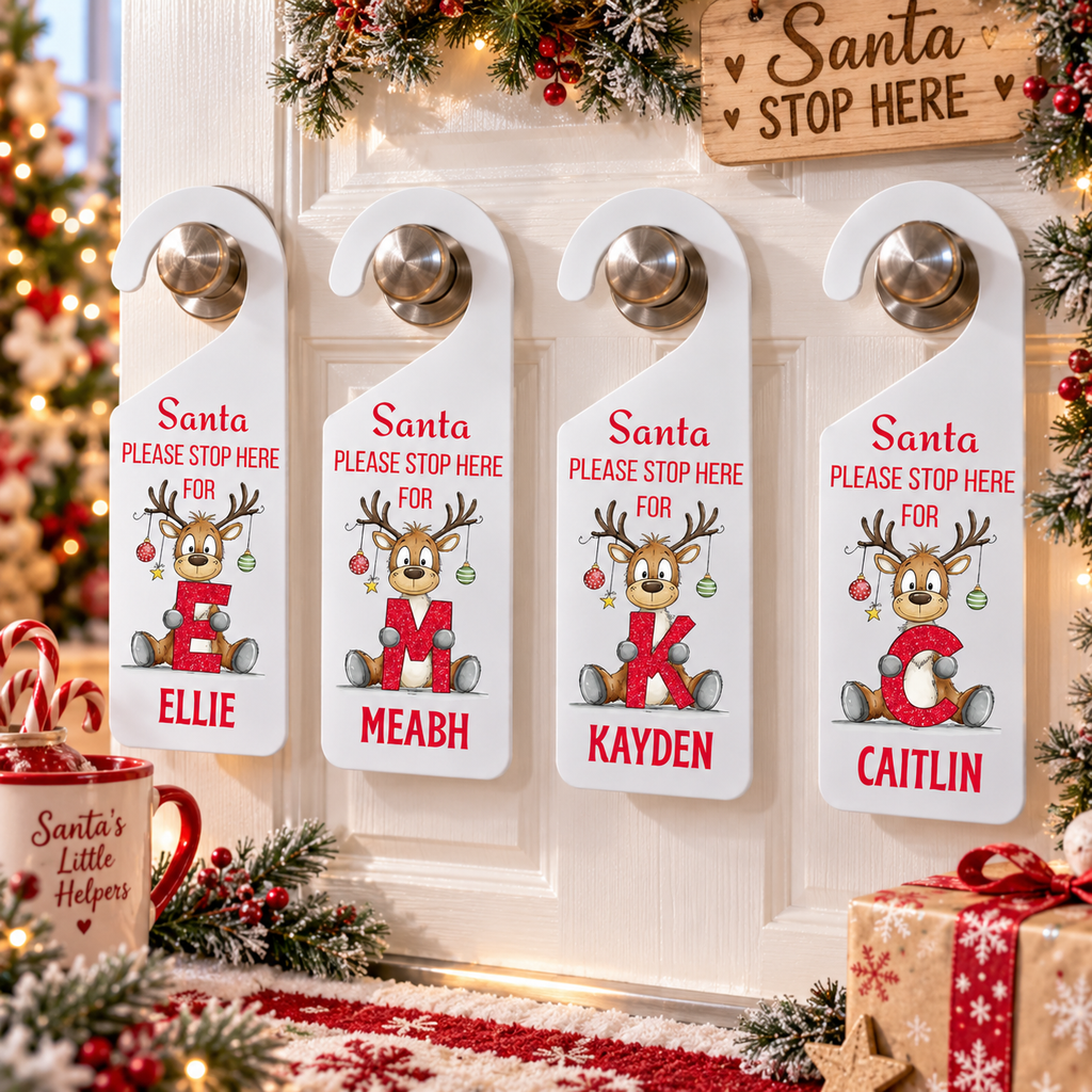 Four personalized Christmas door hangers with silver doorknobs displayed on a white door decorated with holiday garlands, a mug, and a gift box.