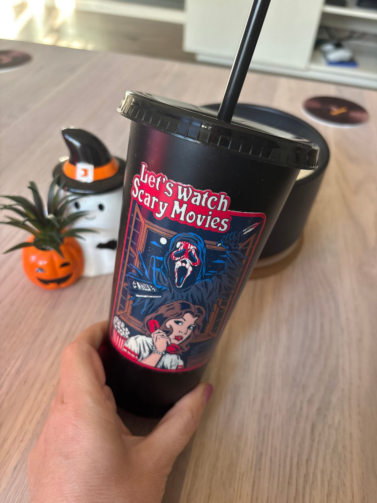 Close-up of black 24oz tumbler with a girl on a red phone and a masked figure at the window