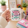 Person holding a mug with 'Teaching Assistant' design in a classroom setting