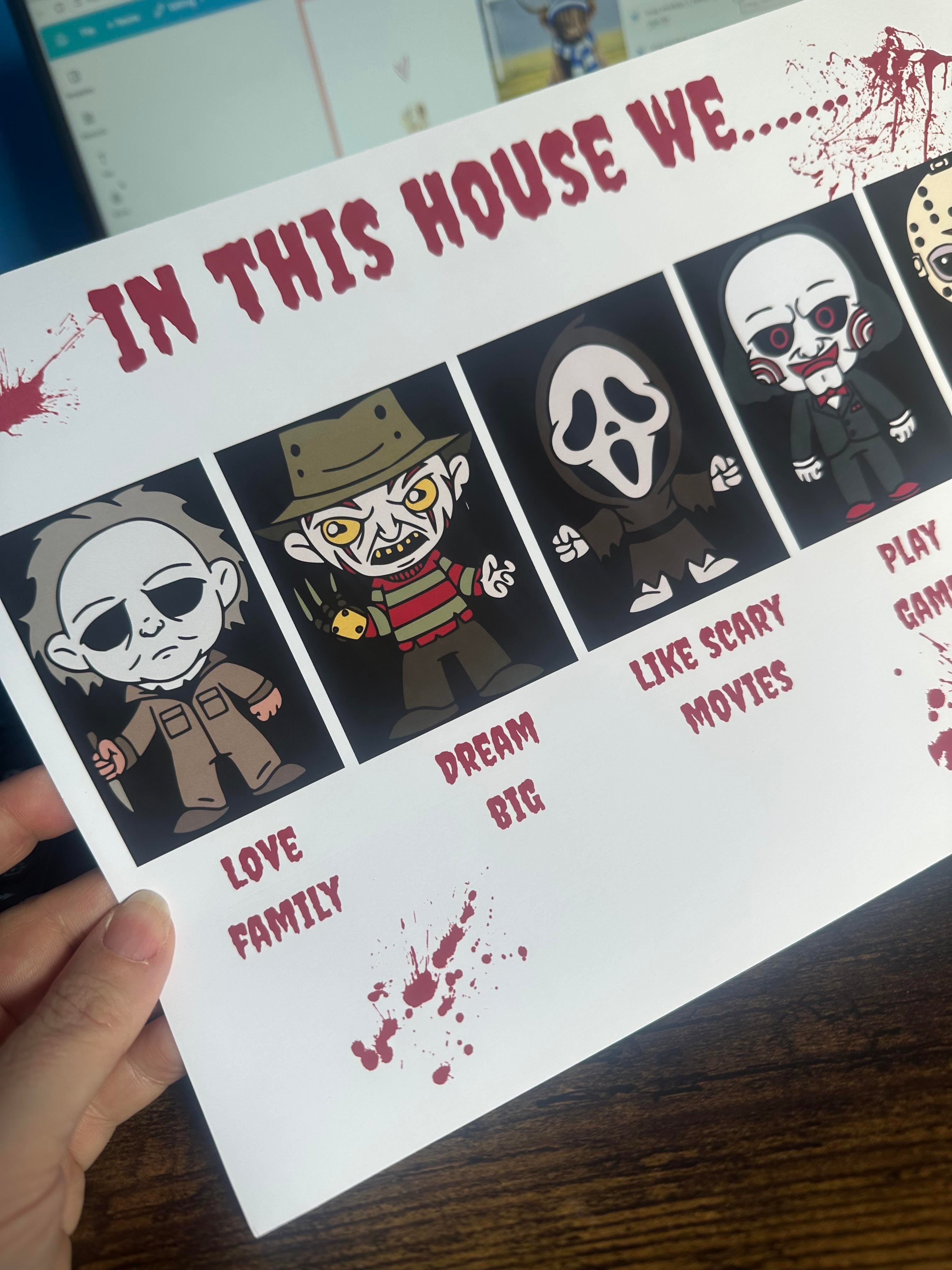 A hand holding a printed white card with horror-themed cartoon illustrations and red text reading 'IN THIS HOUSE WE.