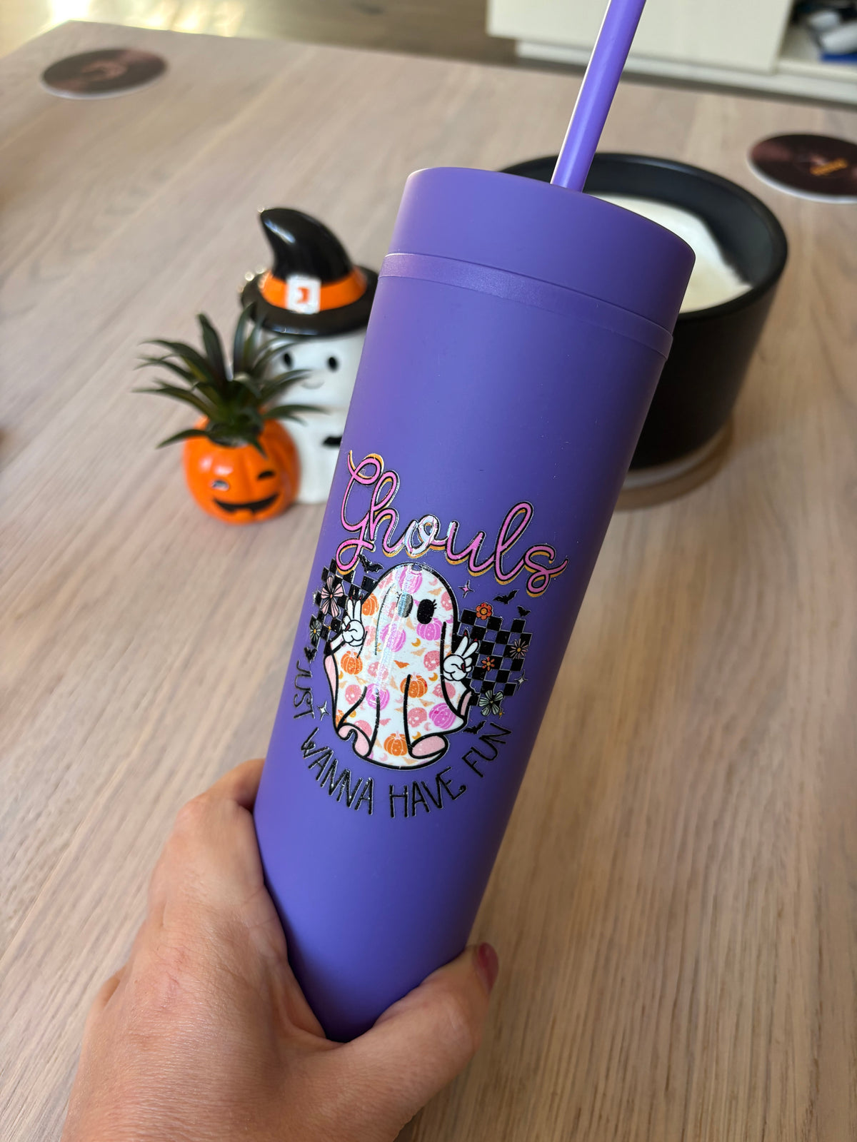 Hand holding a purple skinny tumbler with a retro ghost, checkerboard and bats design that shows its slim size