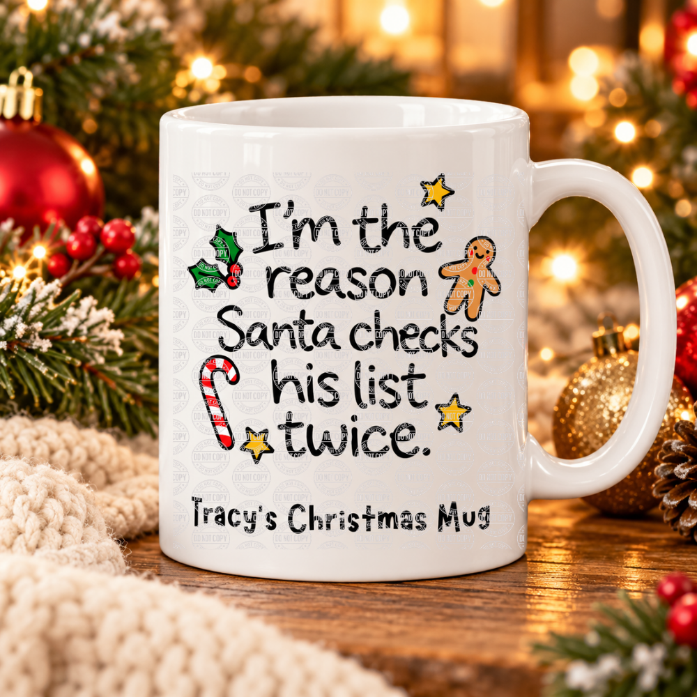 A white ceramic mug with a Christmas-themed printed message reading 'I'm the reason Santa checks his list twice.' and 'Tracy's Christmas Mug,' styled on a wooden surface with holiday greenery, ornaments, and warm blurred lights in the background.