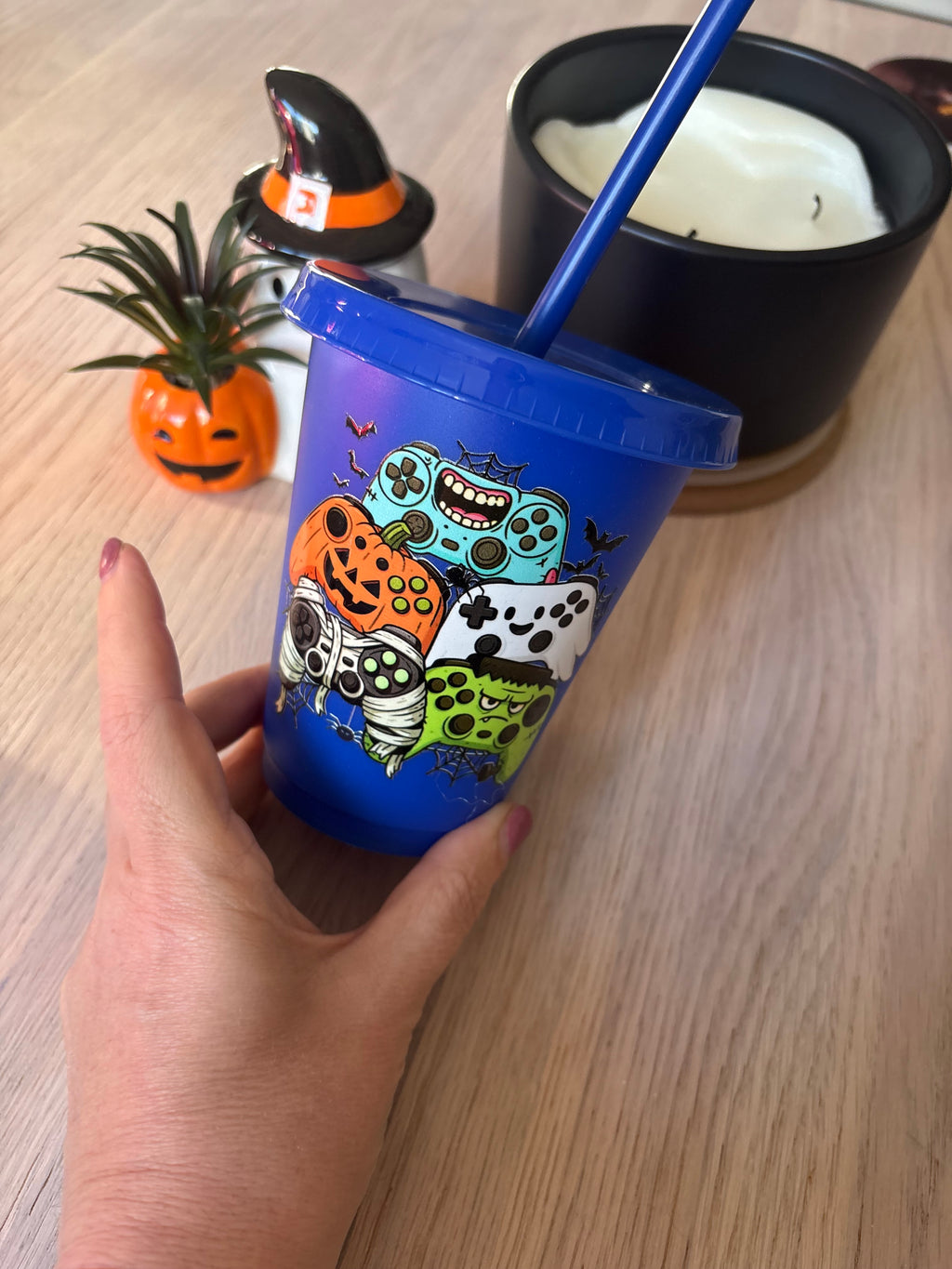 Close-up of Halloween gaming controllers styled as a pumpkin, mummy, ghost and monster with bats and cobwebs on a blue cup