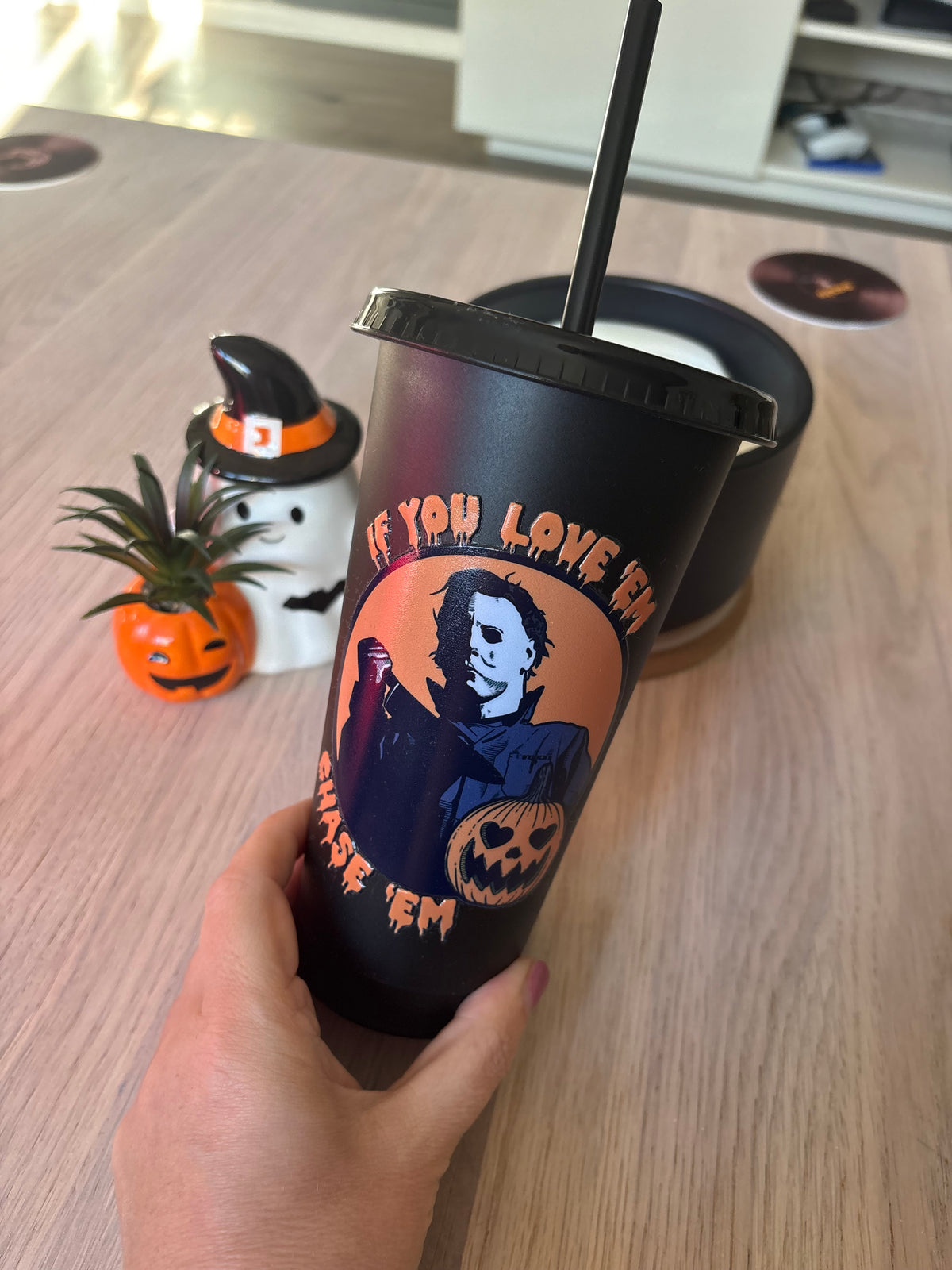 Close-up of masked slasher holding a knife beside a heart-eyed pumpkin on a black tumbler