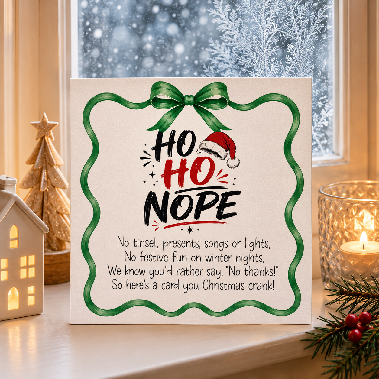 A square Christmas greeting card with the phrase 'Ho Ho Nope' and a poem printed on it, styled on a windowsill with a lit candle, a small house ornament, and pine branches nearby.