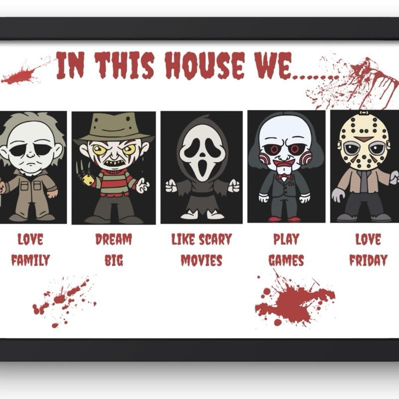 A framed horror-themed print featuring five cartoon characters labeled Love Family, Dream Big, Like Scary Movies, Play Games, and Love Friday, with red splatter graphics and the text 'IN THIS HOUSE WE.