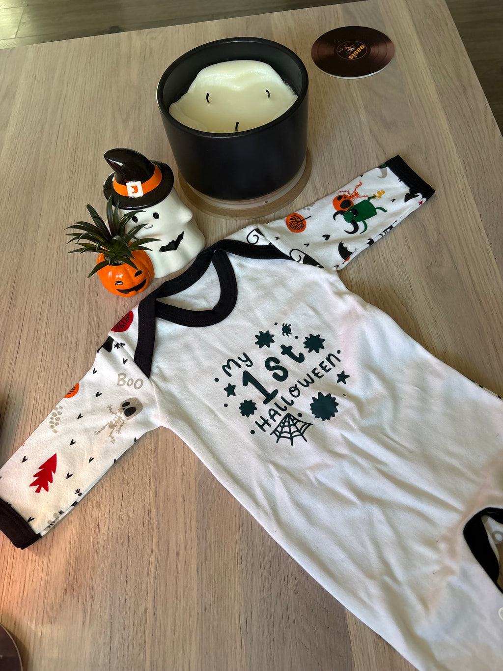 Baby Halloween sleepsuit laid flat beside a ghost and pumpkin Halloween decorations