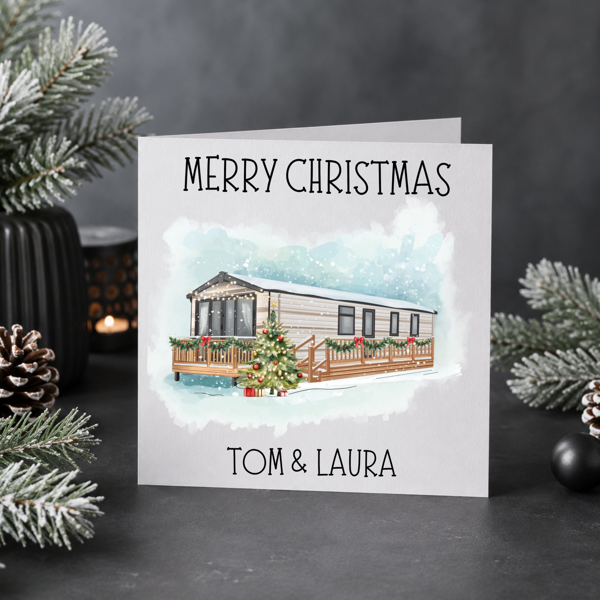 A personalized Christmas greeting card with a watercolor illustration of a caravan on a deck, surrounded by holiday decorations like pine branches and a candle on a dark gray background.