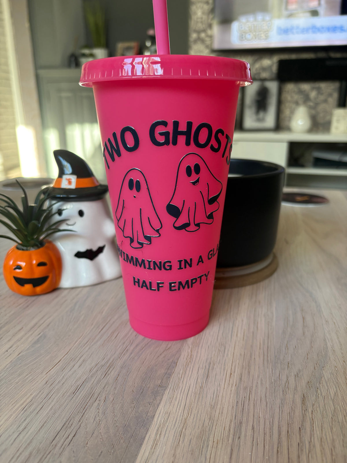 Hot pink 24oz ghost cold cup with lid and straw, black vinyl design of two cartoon ghosts and “glass half empty” text