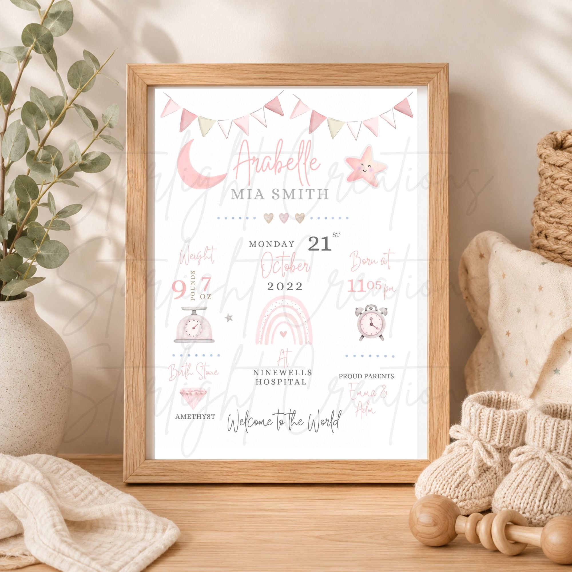 A framed baby shower print featuring a personalized name 'Aubrey' and 'Mia Smith' with pastel illustrations of a crescent moon, star, rainbow, and bunting, styled on a wooden surface with baby shoes, a blanket, and a vase of greenery.
