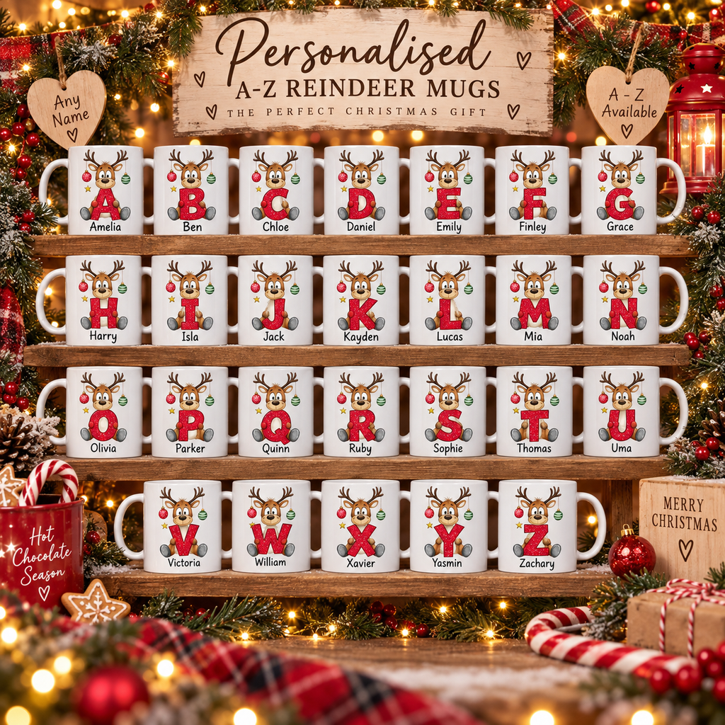 A set of personalized A-Z reindeer mugs displayed on wooden shelves under a decorative sign reading 'Personalised A-Z Reindeer Mugs'. The white ceramic mugs each feature a colorful reindeer illustration with a letter from A to Z, holiday decorations, and the mug name printed on the side.