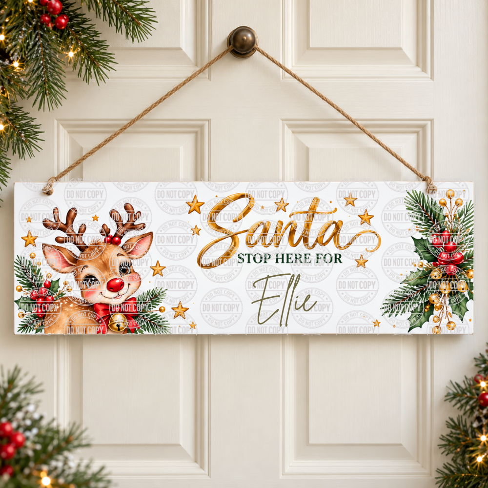 A personalized Christmas hanging sign with a white background, gold glittery 'Santa' script, 'STOP HERE FOR Ellie' text, and holiday illustrations including a reindeer and green pine garlands with red ornaments. The sign hangs from a rope on a cream-colored paneled door, framed by festive greenery and lights at the corners.