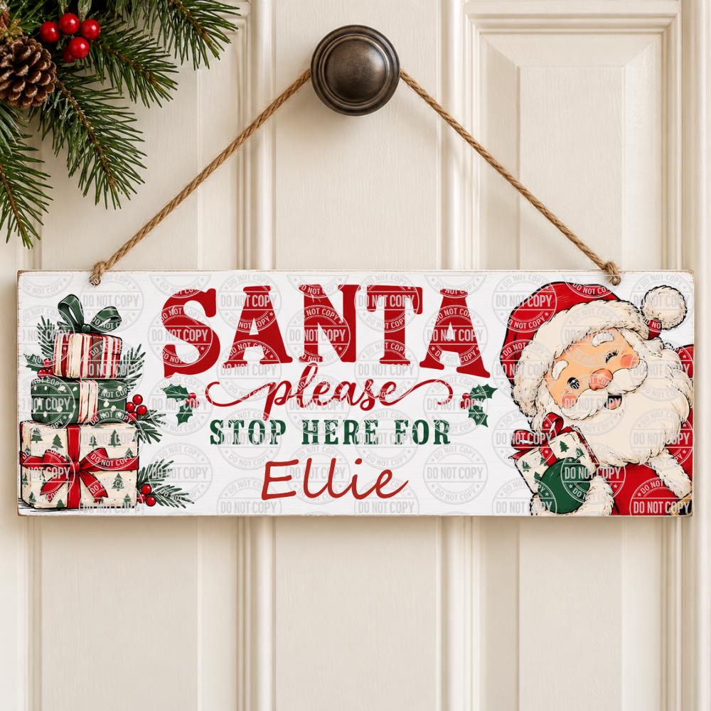 A rectangular Christmas hanging sign with a rope handle, featuring the text 'SANTA please STOP HERE FOR Ellie' in red and green lettering, along with illustrations of wrapped gifts, holly, pinecones, and a smiling Santa Claus on a white paneled door background.