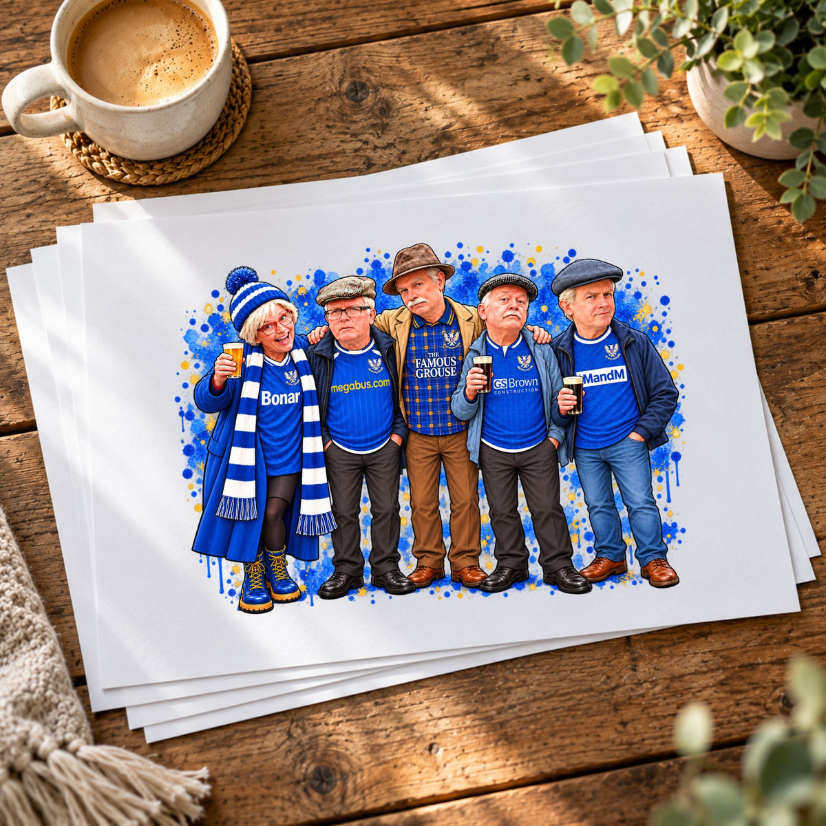 A stack of custom watercolor art prints featuring five men in blue football jerseys, displayed on a rustic wooden table next to a coffee cup.