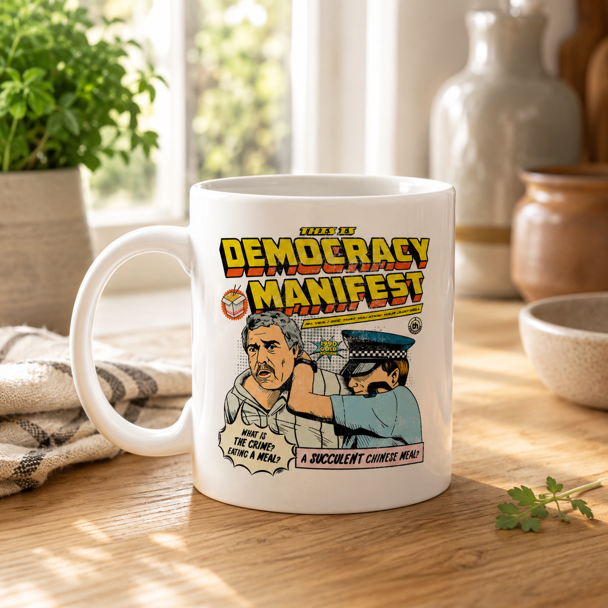 A white ceramic mug with a colorful retro-style graphic print reading 'Tired of Democracy Manifest' and an illustration, placed on a wooden table in a bright kitchen setting.