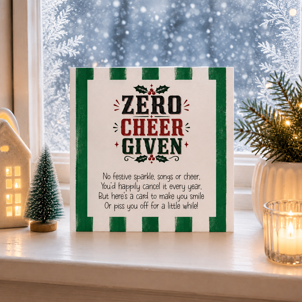 A square Christmas sign with the text 'ZERO CHEER GIVEN' and a poem below, styled on a windowsill with holiday decor including a small tree, a glowing house, and a candle.